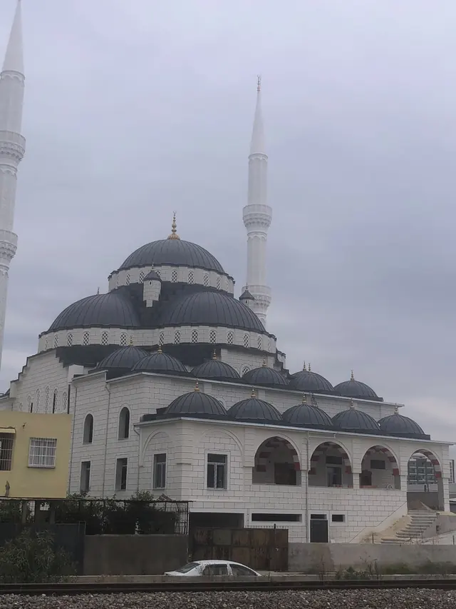 Antrasit renkli metal kaplı ana kubbe, kademeli yarım kubbeler ve iki minareli cami