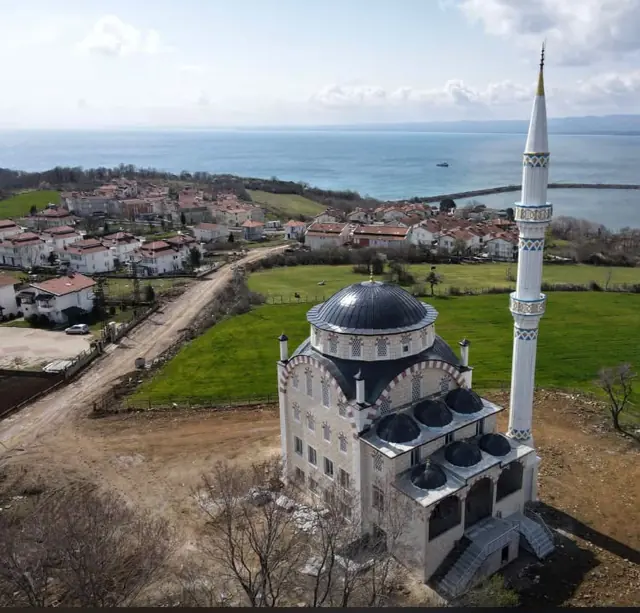 Deniz kenarındaki köyde antrasit kubbe ve kubbecikleriyle tek minareli cami, havadan görünüm