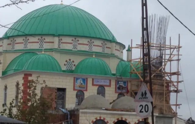 Yeşil kaplanmış ana kubbe ve yarım kubbeler, yanında iskele kurulmuş minare